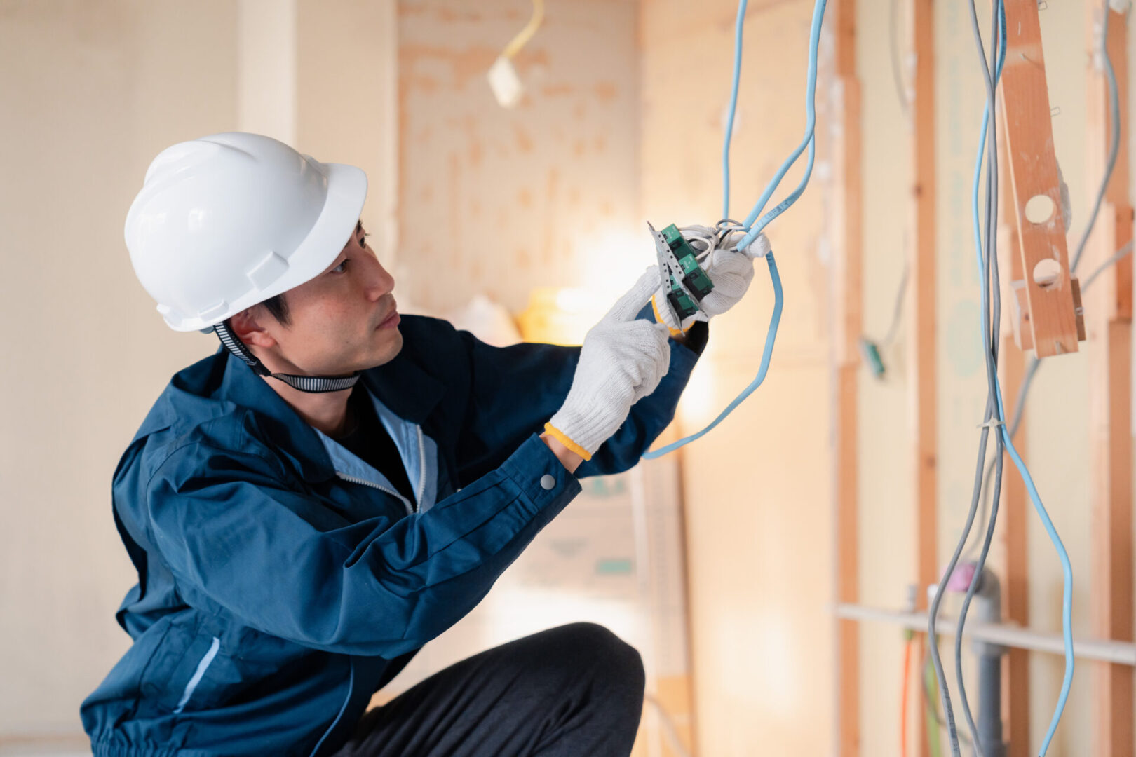 Electrician working on wiring at construction site An electrician in a hard hat and gloves expertly installs wiring in a partially finished wall, adeptly troubleshooting electrical issues as they arise.
