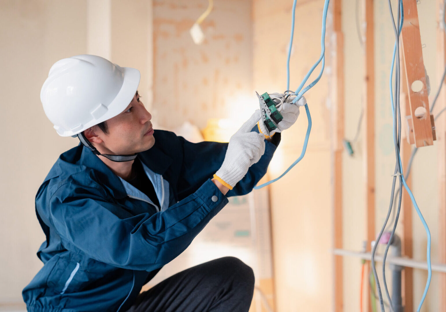 An electrician in a hard hat and gloves expertly installs wiring in a partially finished wall, adeptly troubleshooting electrical issues as they arise.
